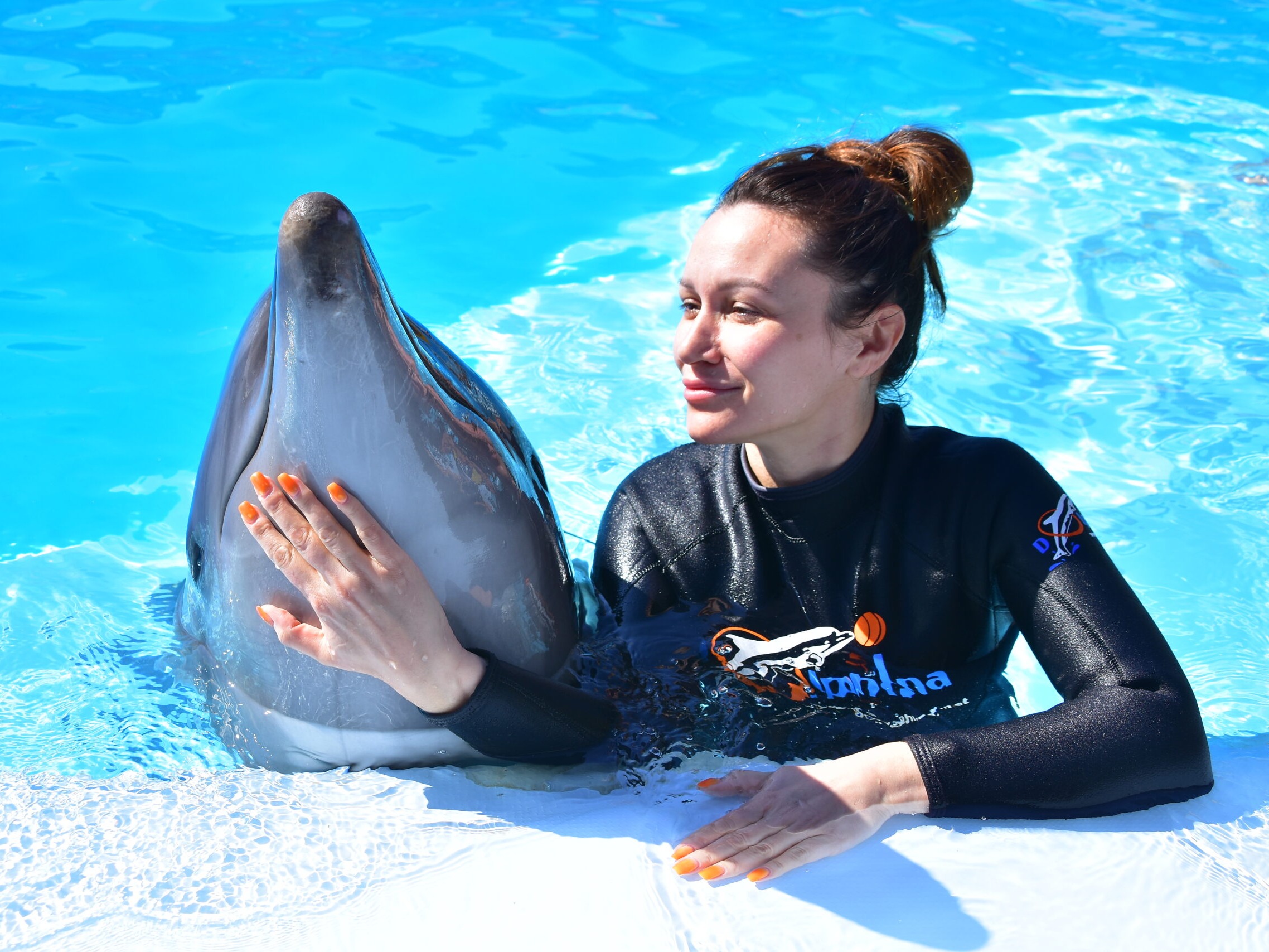Gast posiert mit einem Delfin im Wasser
