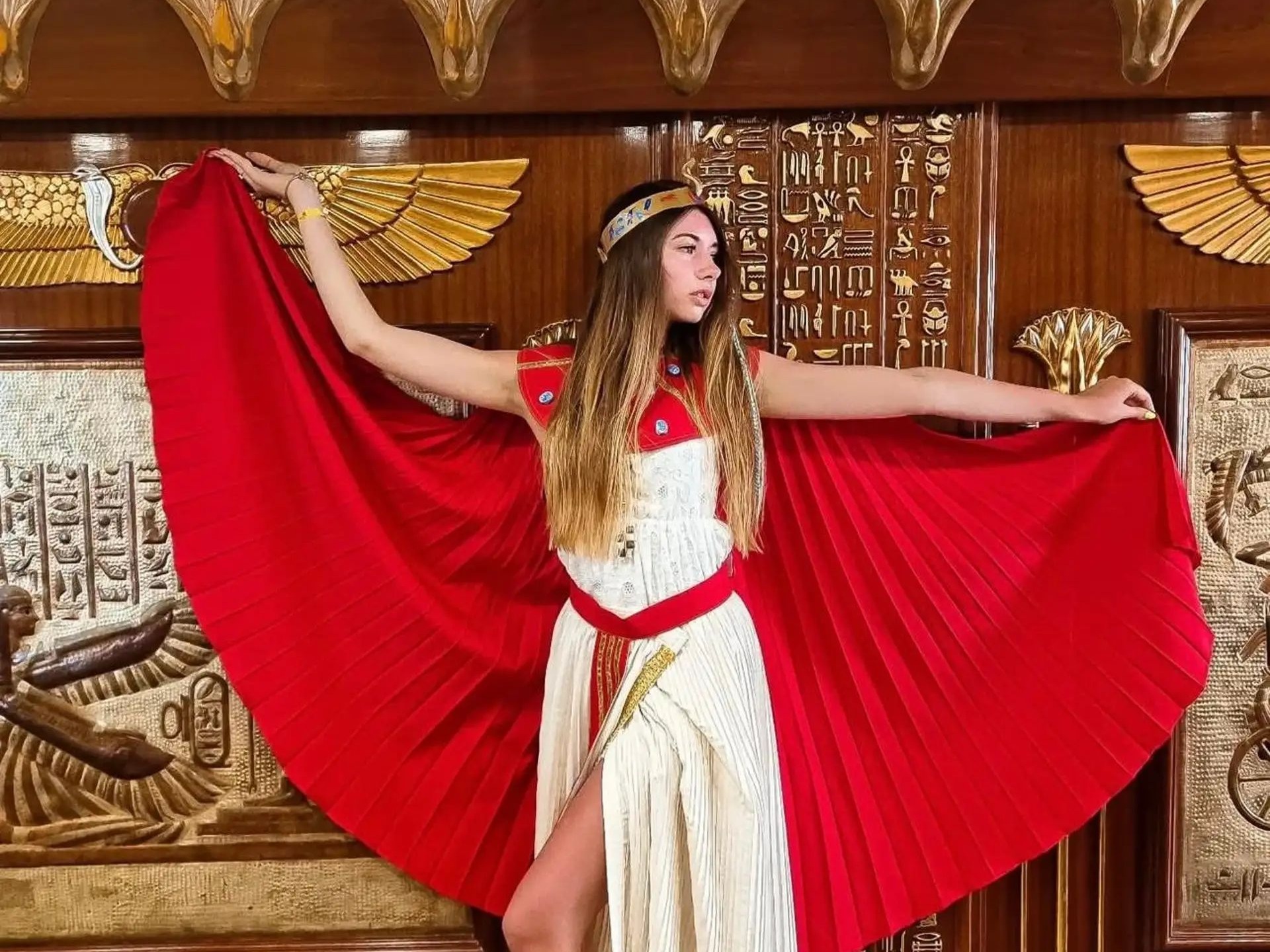 Woman in Egyptian queen costume posing against hieroglyphic background