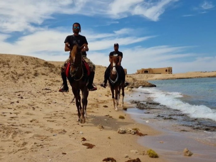 Two riders on horses along a quiet coastal desert