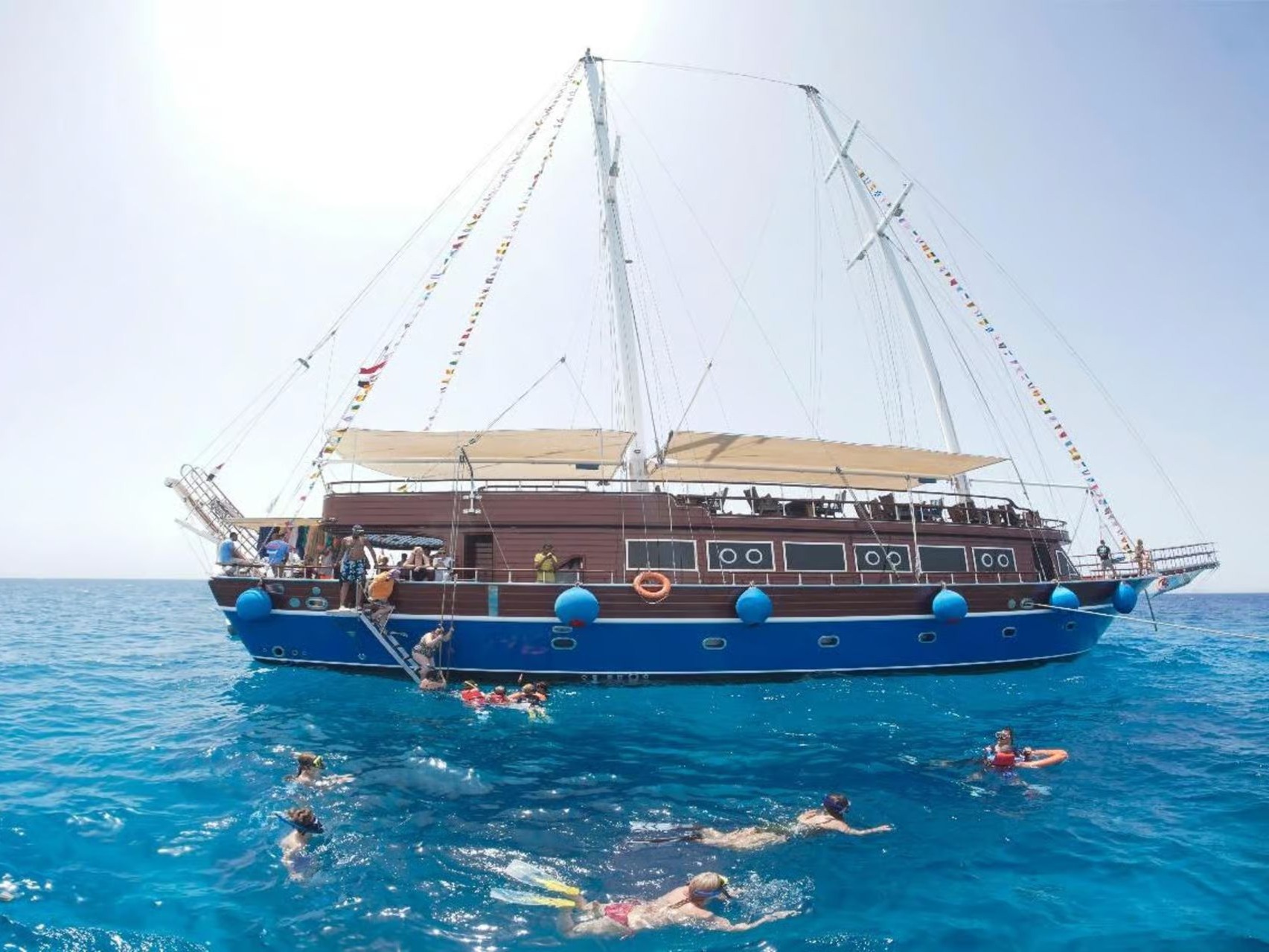 Pirate-style sailing boat anchored with people snorkeling in the sea